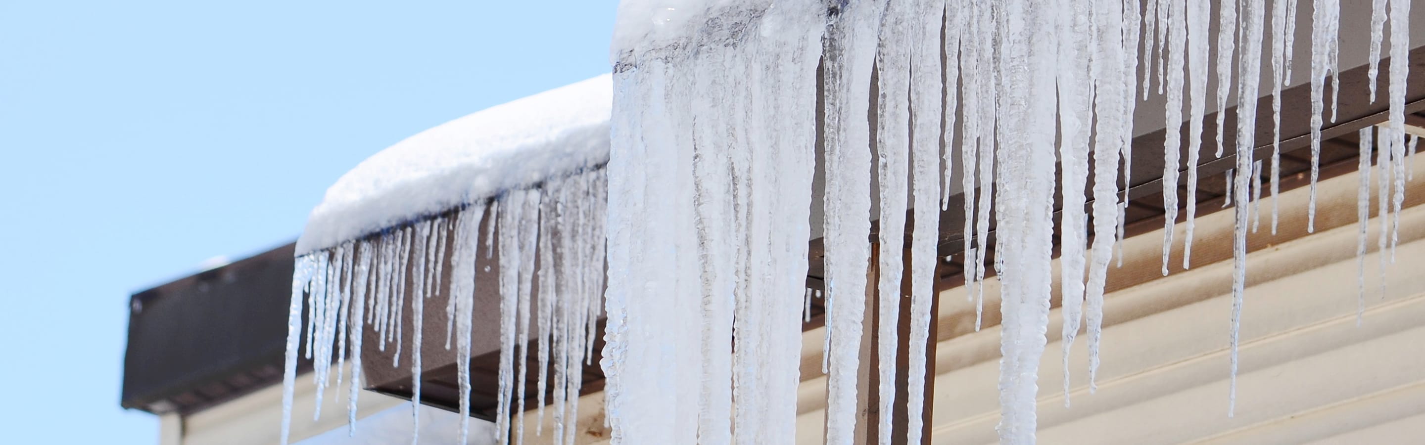 Heavy icicles hanging from a roof and gutters covered in ice.