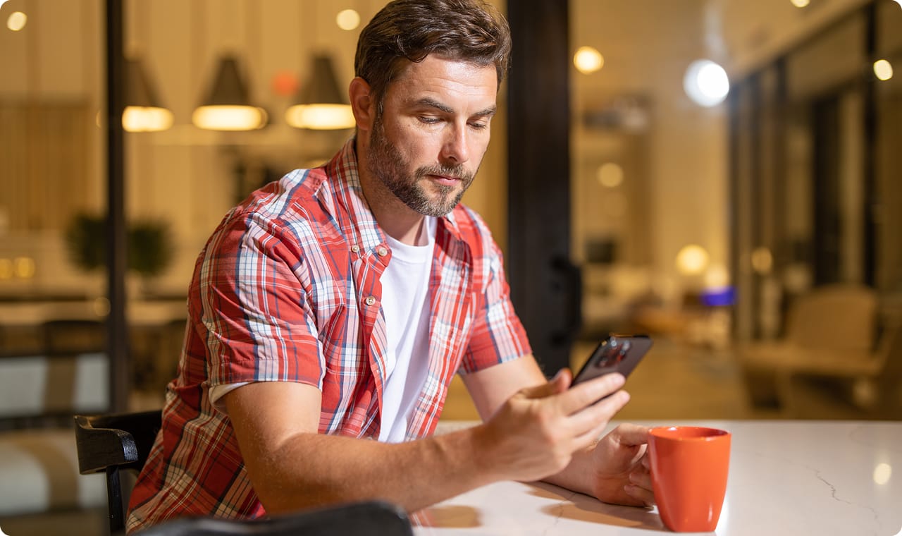 Man sitting at a table looking at his phone in a dimly lit room.