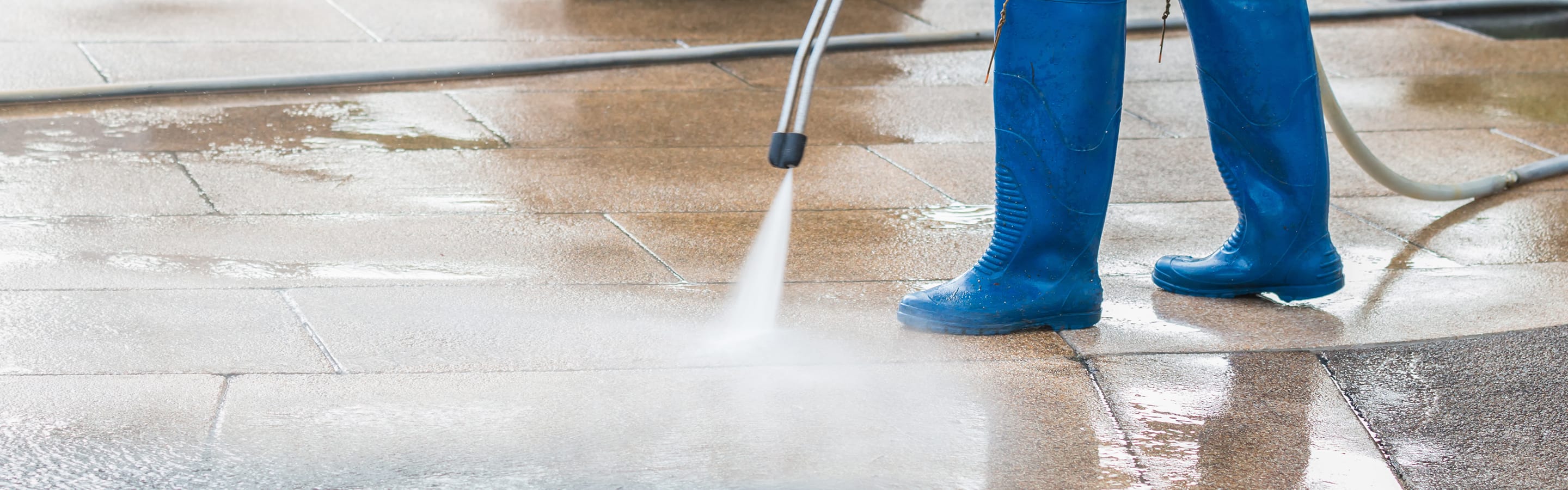 Person power washing an oil-stained concrete driveway.
