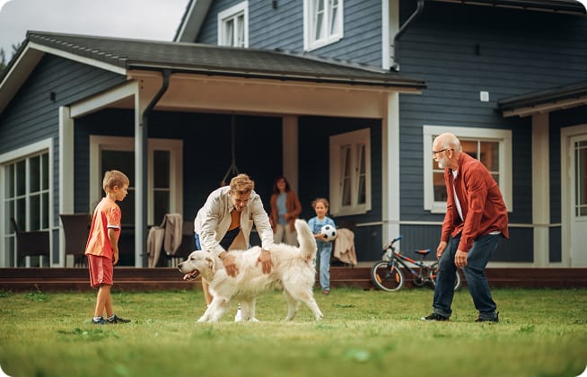 Multi-generational family playing with a dog in the front yard of a home.