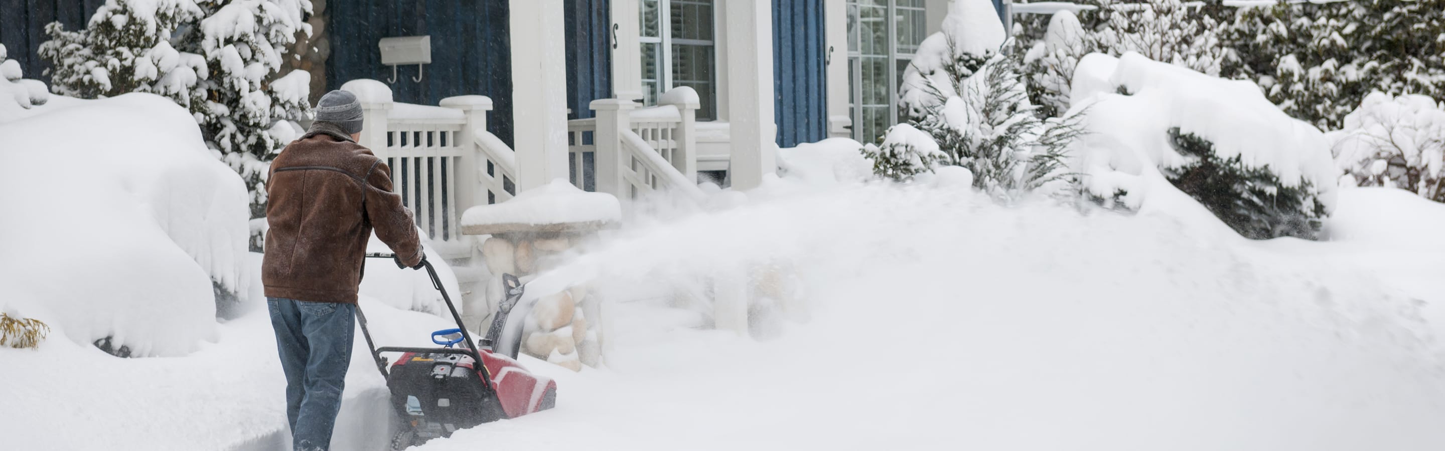 Person using a snow blower to clear a heavily snow-covered front yard.