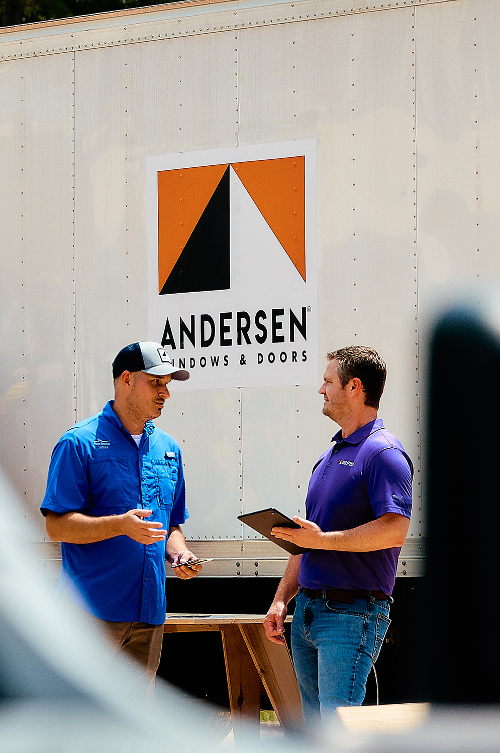 Two men chatting in front of an Andersen Windows truck