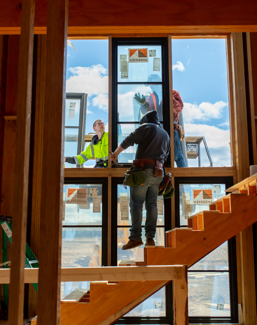Builders installing large Andersen windows above a stairway