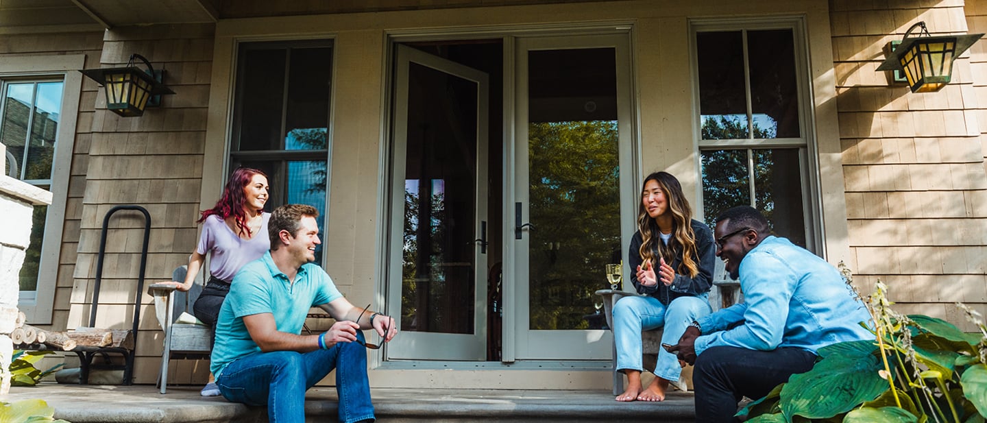 Four people sitting outside patio door on steps talking