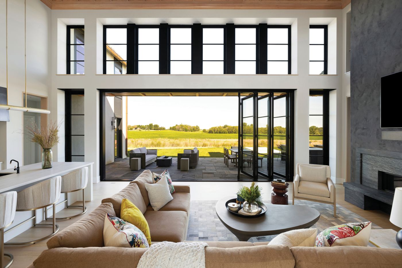 An open six panel Folding Outswing Door with black frames, black horizontal grilles, transoms, and sidelights in a large living room with a tan couch. 