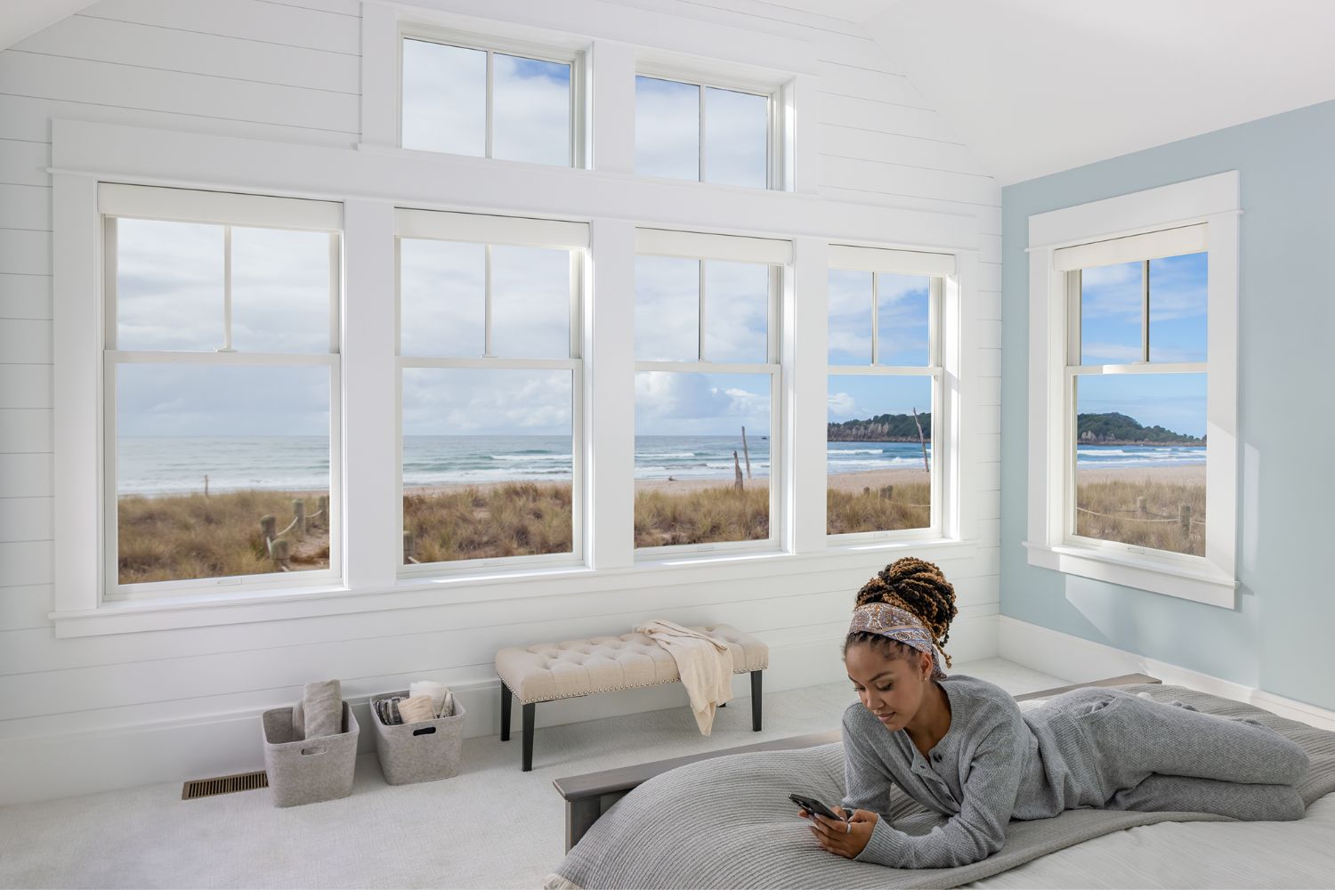 White coastal impact windows by Renewal by Andersen fill a bright beach house bedroom with natural light, showcasing expansive ocean views and durable coastal window design built for seaside homes.