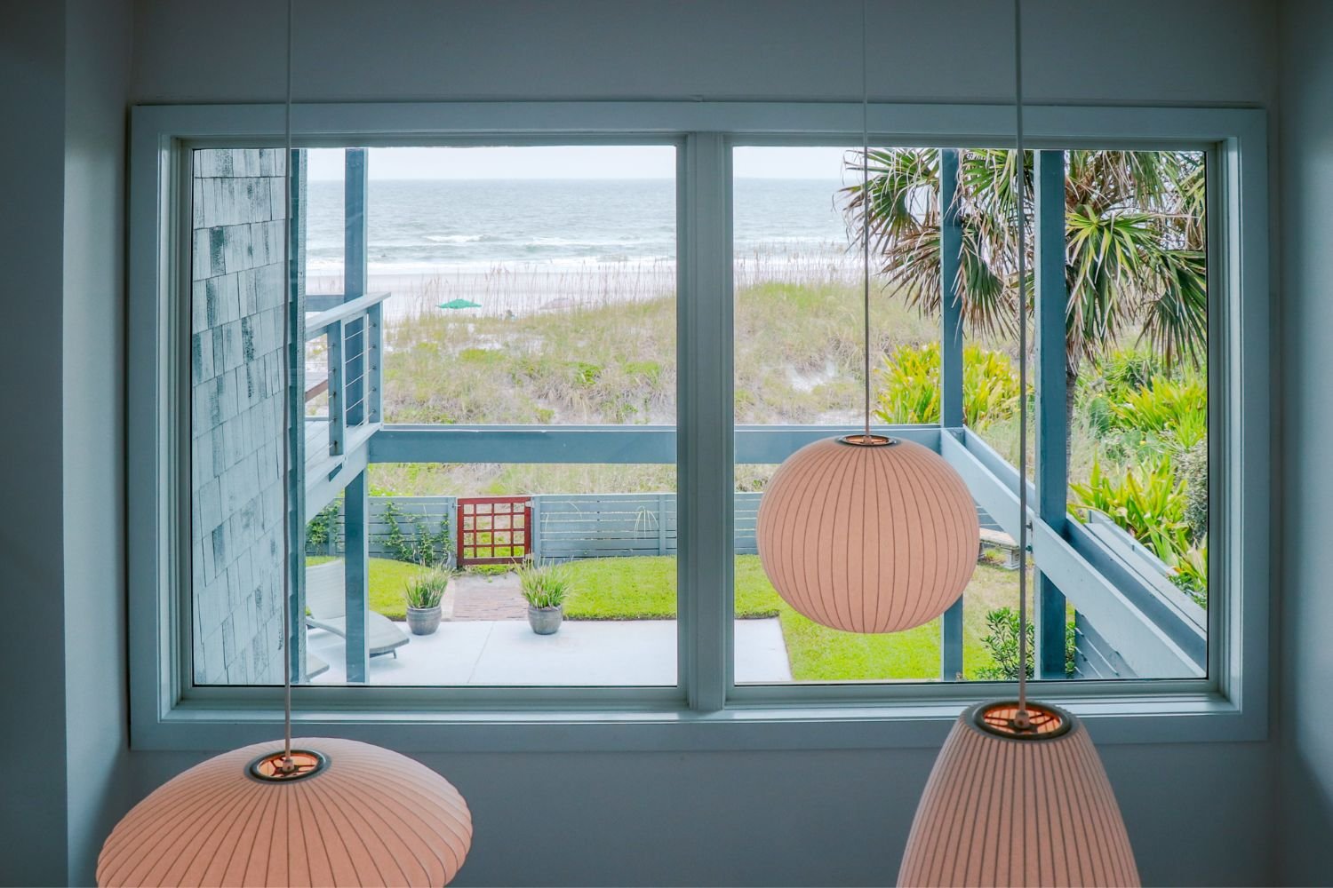 Large coastal picture windows frame ocean and dune views from a beachfront home, bringing natural light indoors while showcasing durable window design for coastal environments.