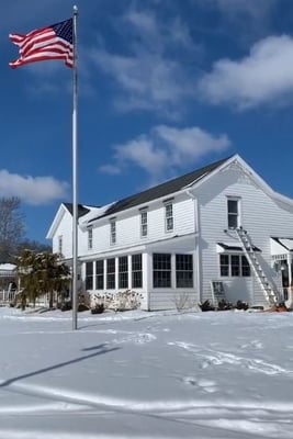 A white farm house with a ladder by it. Certified master installers are putting in windows in the winter.