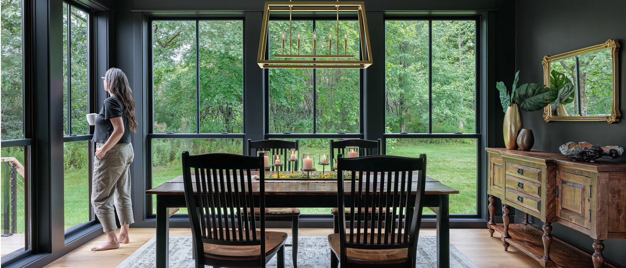 A woman standing in a bright dining room beside a wall of replacement windows