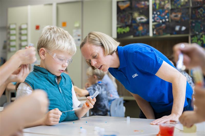 Kind en ASML Junior Academy-begeleider buigen zich over een proefje aan tafel.