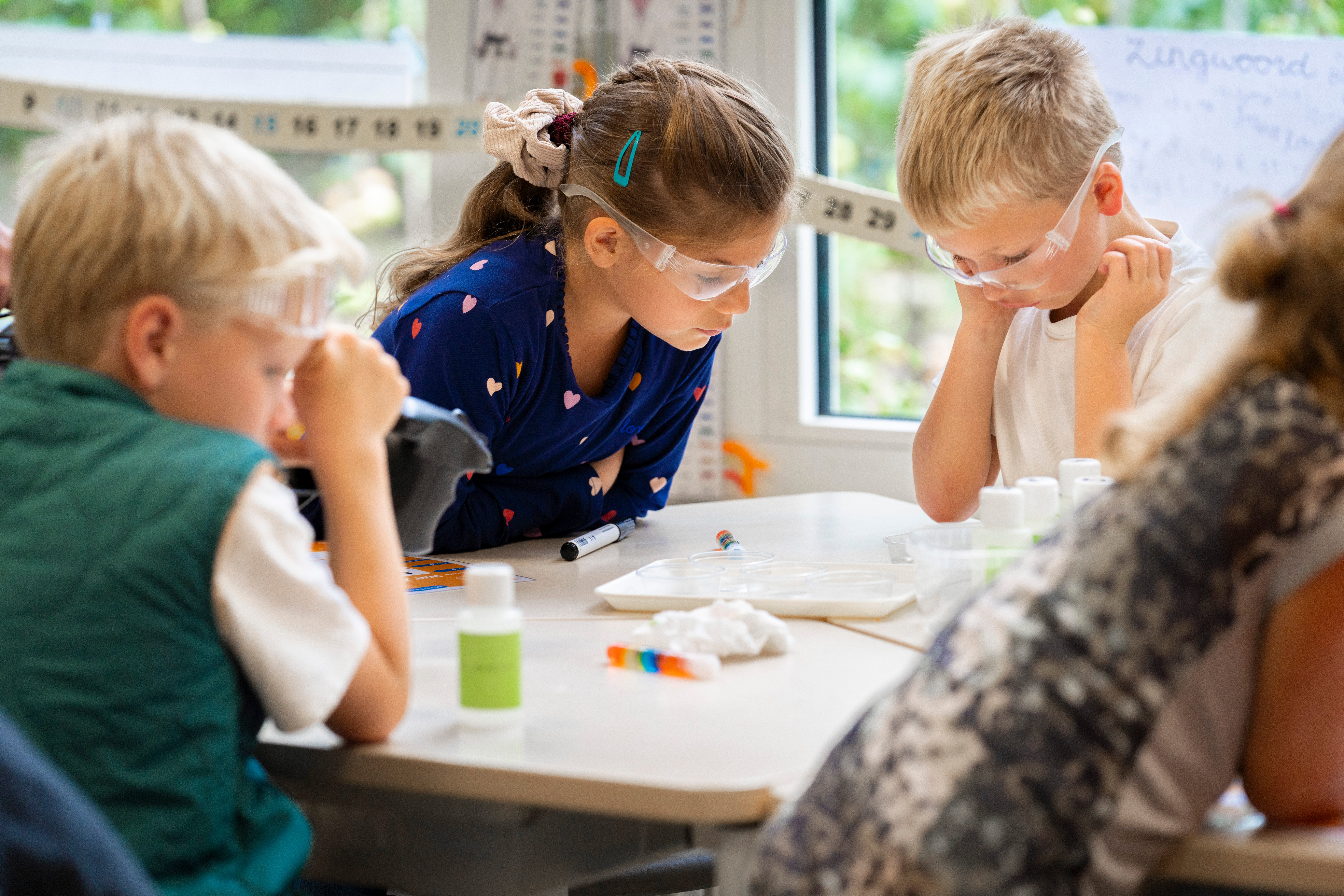 Groep kinderen met veiligheidsbrillen werkt geconcentreerd aan een proefje bij ASML Junior Academy.