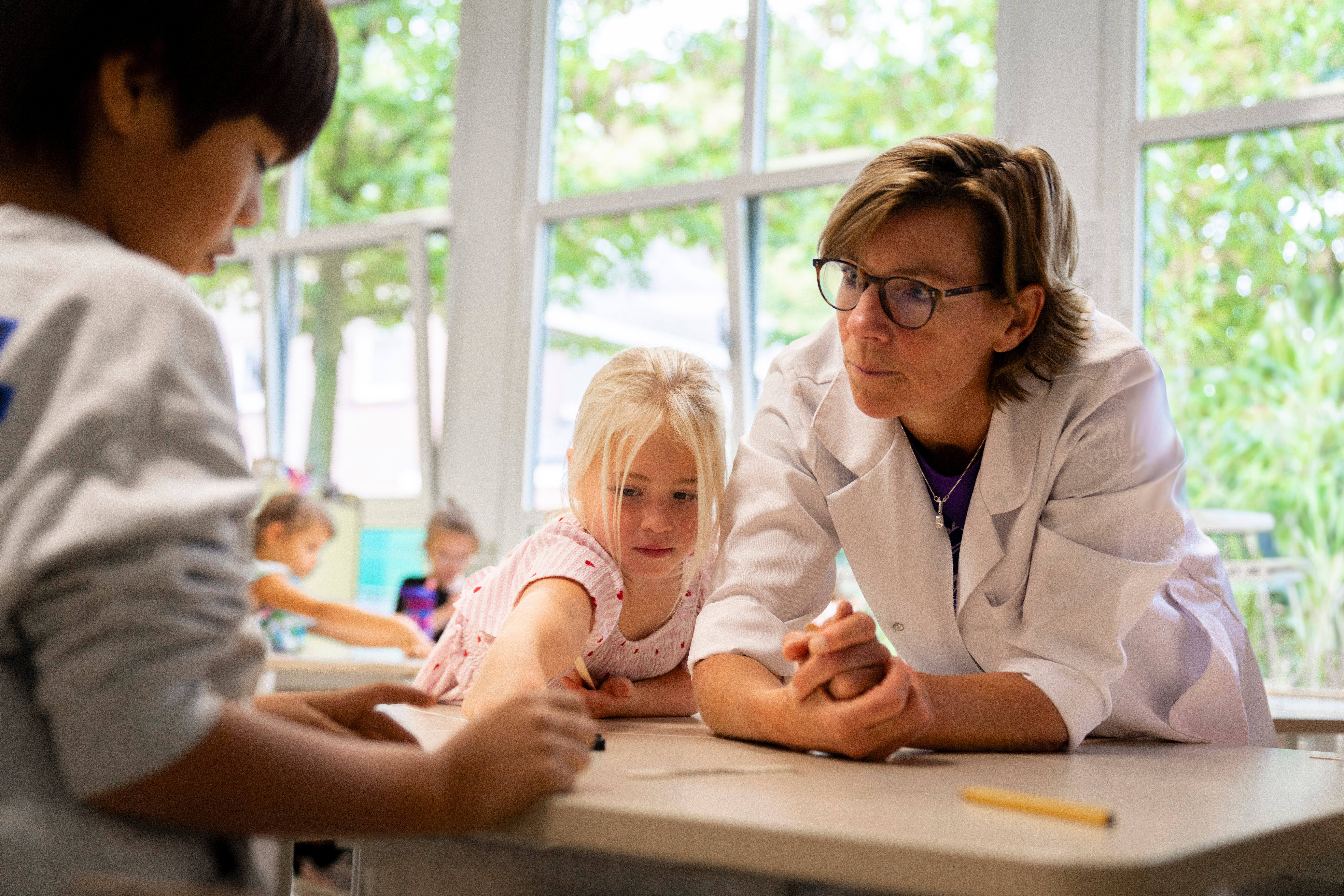 Begeleider van ASML Junior Academy kijkt mee met kinderen tijdens een klaslokaalexperiment.