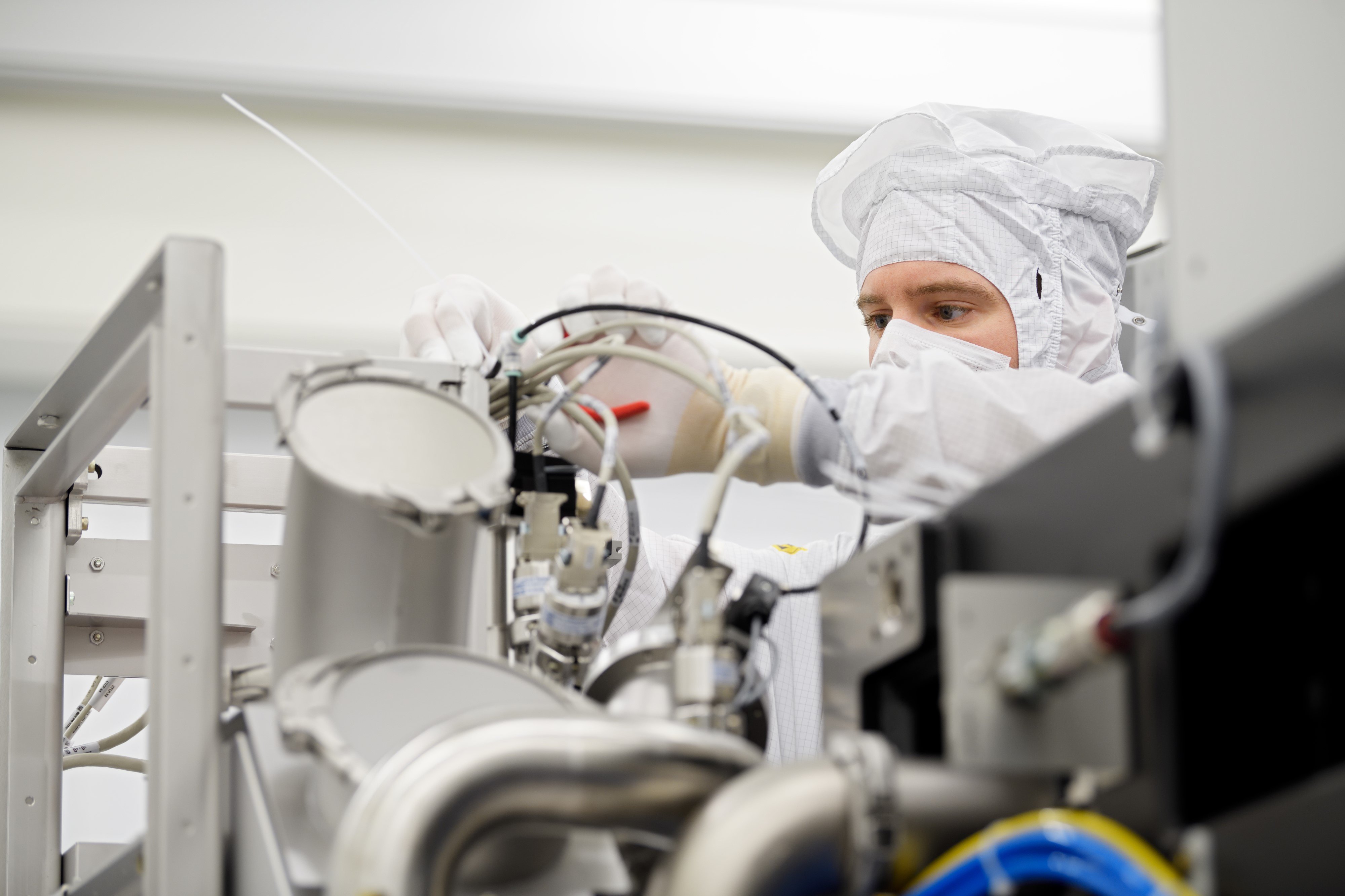 Een ASML medewerker draagt een cleanroom pak en werkt aan een geavanceerde machine.