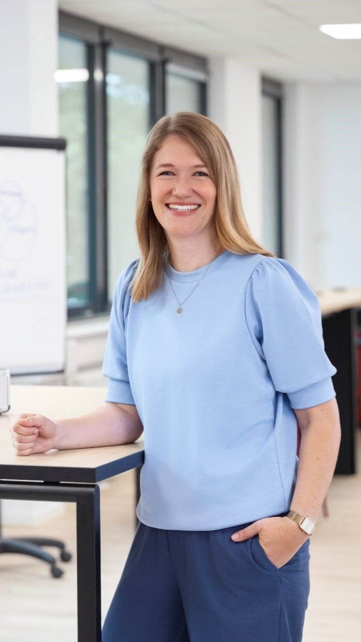 Eine Frau steht an einem Tisch mit einem Moderationskoffer und einem Flipchart im Hintergrund