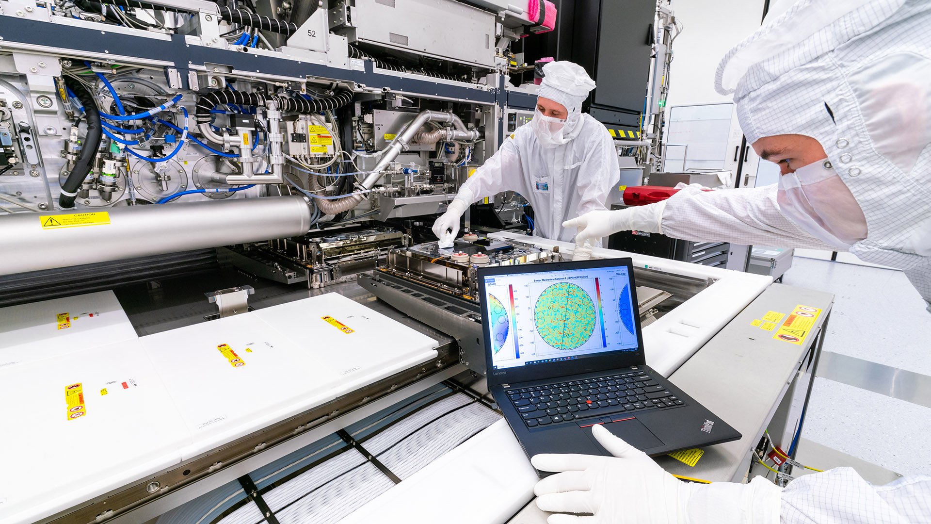 Two ASML engineers in white cleanroom suits use a laptop to test an EUV lithography machine in our factory in Veldhoven, the Netherlands.