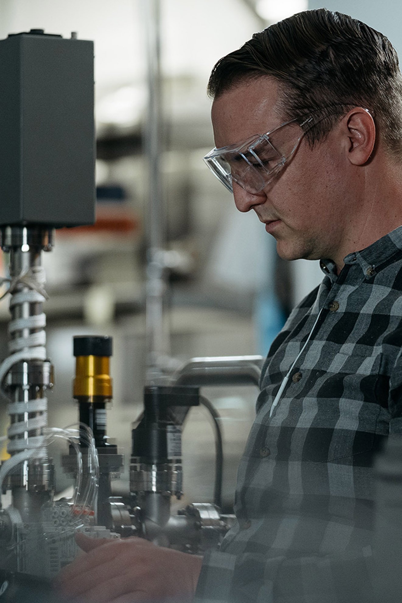 An ASML staff member in safety glasses works on a computer surrounded by machines. 