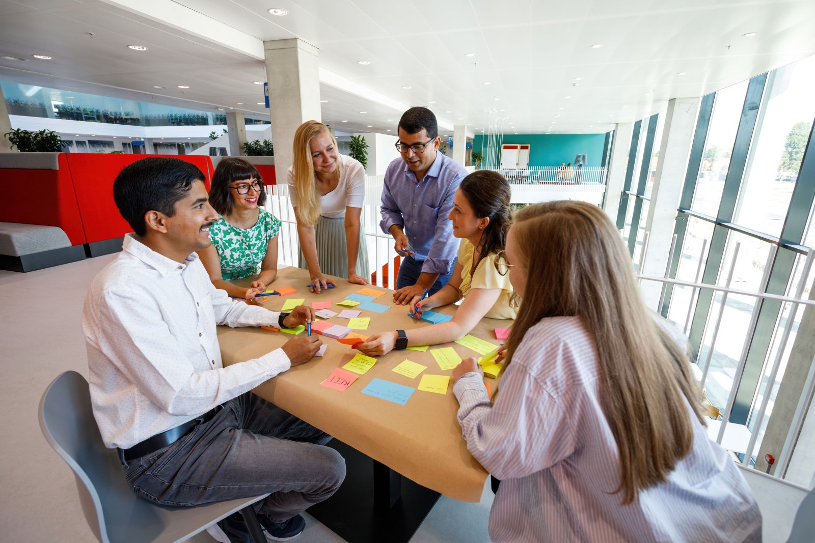 People sitting around a table and smiling, the table has post-its on it. People sitting around a table and smiling, the table has post-its on it.