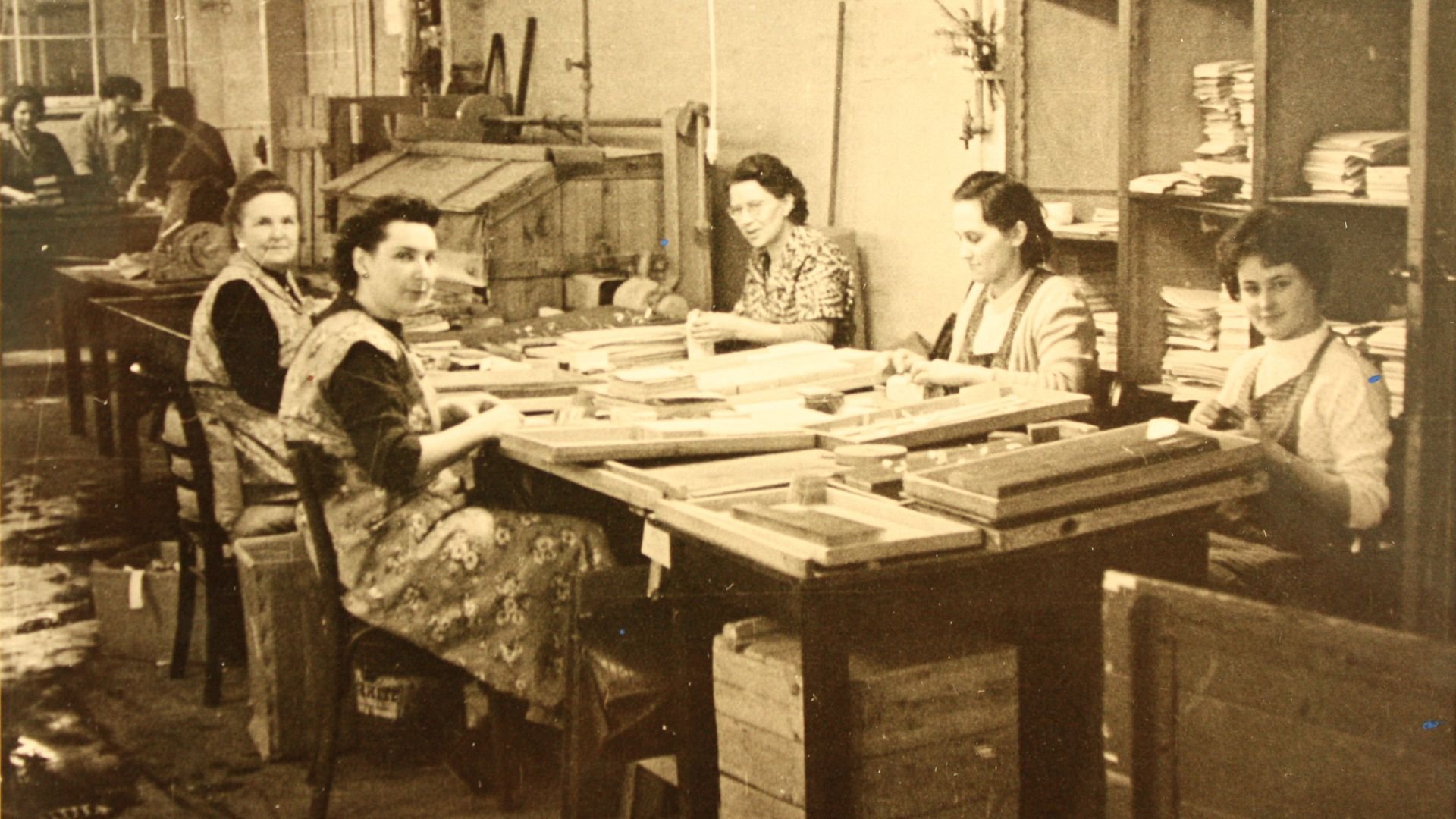 Old-fashioned image of women at a table in a work room.