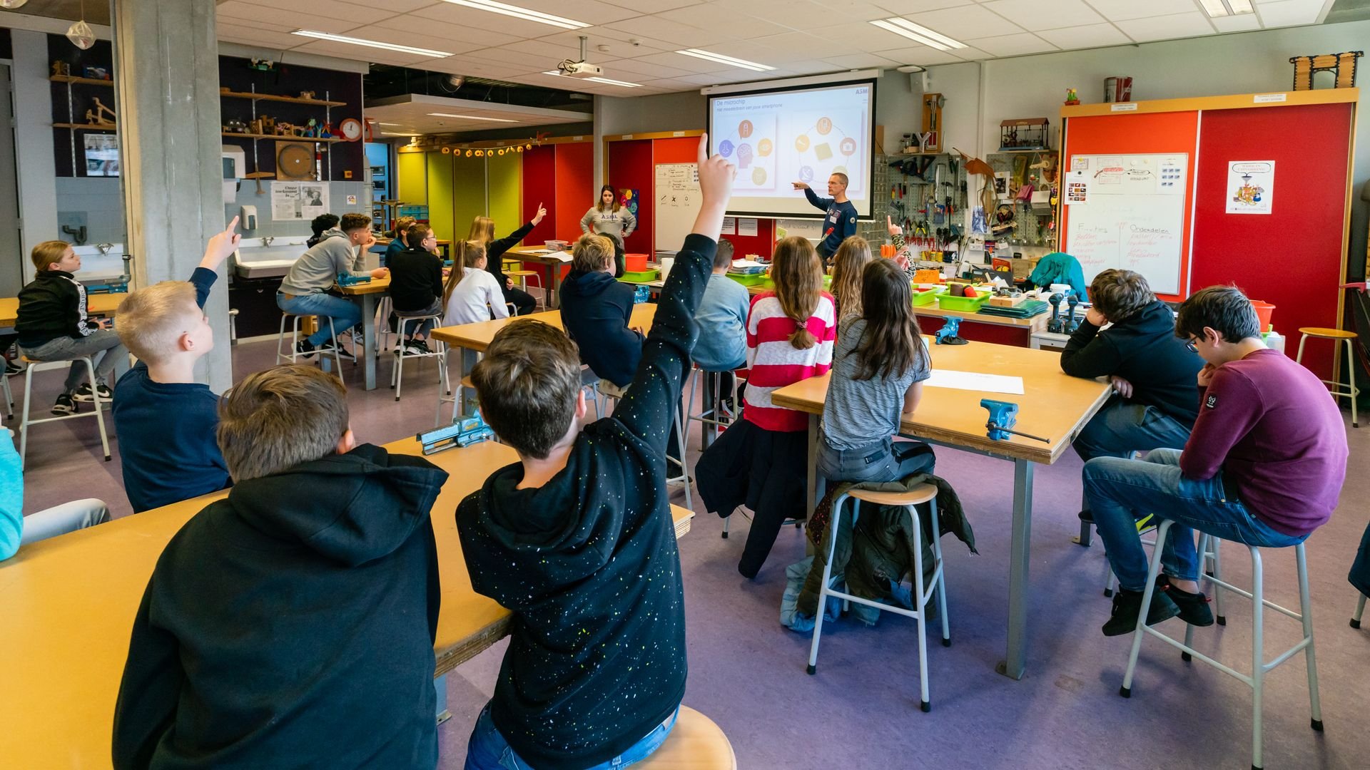 Children in a STEM classroom raise their hands in response to a teacher.