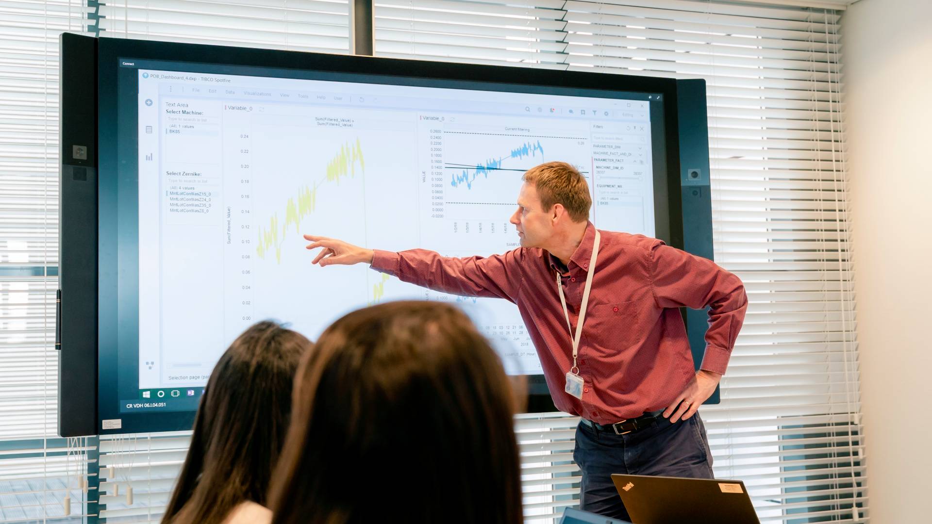 A senior ASML project manager wearing a red shirt presents data insights during a meeting.