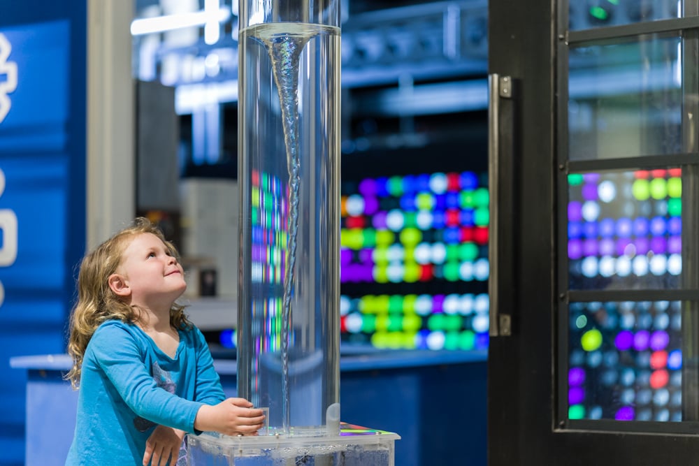 young girl staring up at water vortex in clear tube