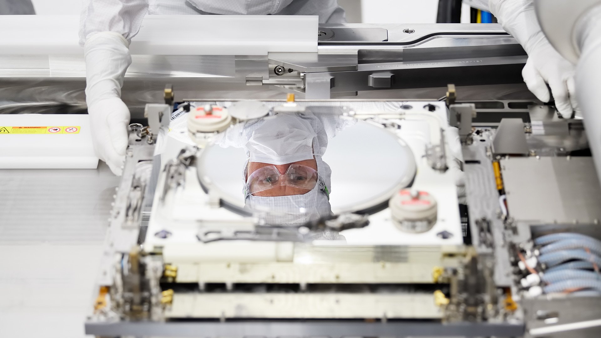 Reflection of engineer in protective clothing looking at silicon wafer