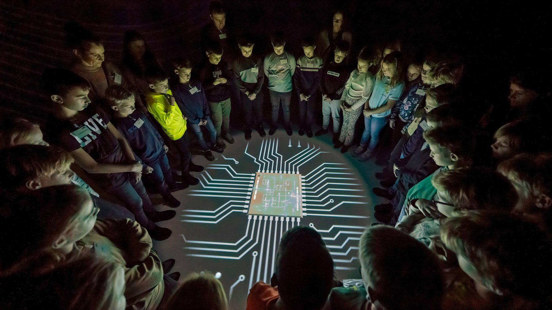 A group of children and adults standing around a projection of a microchip