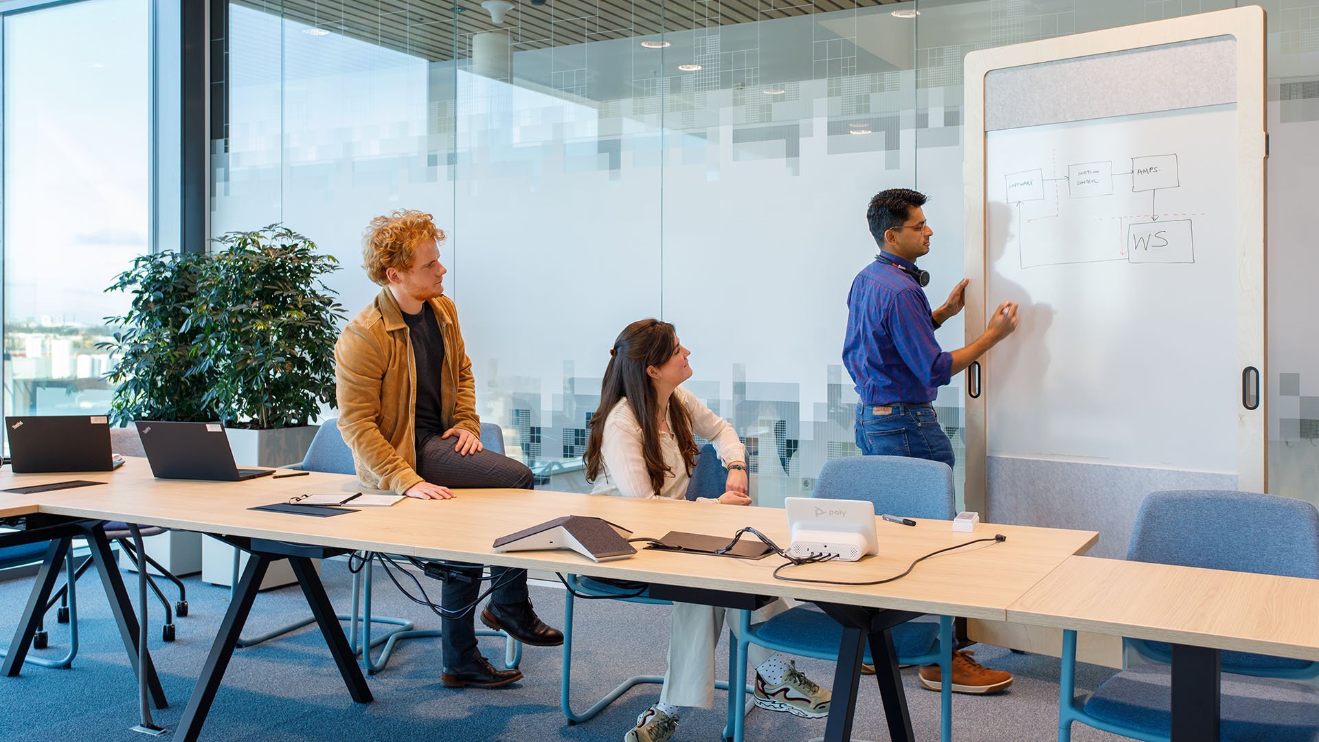 Two seated people watching another person write on a whiteboard