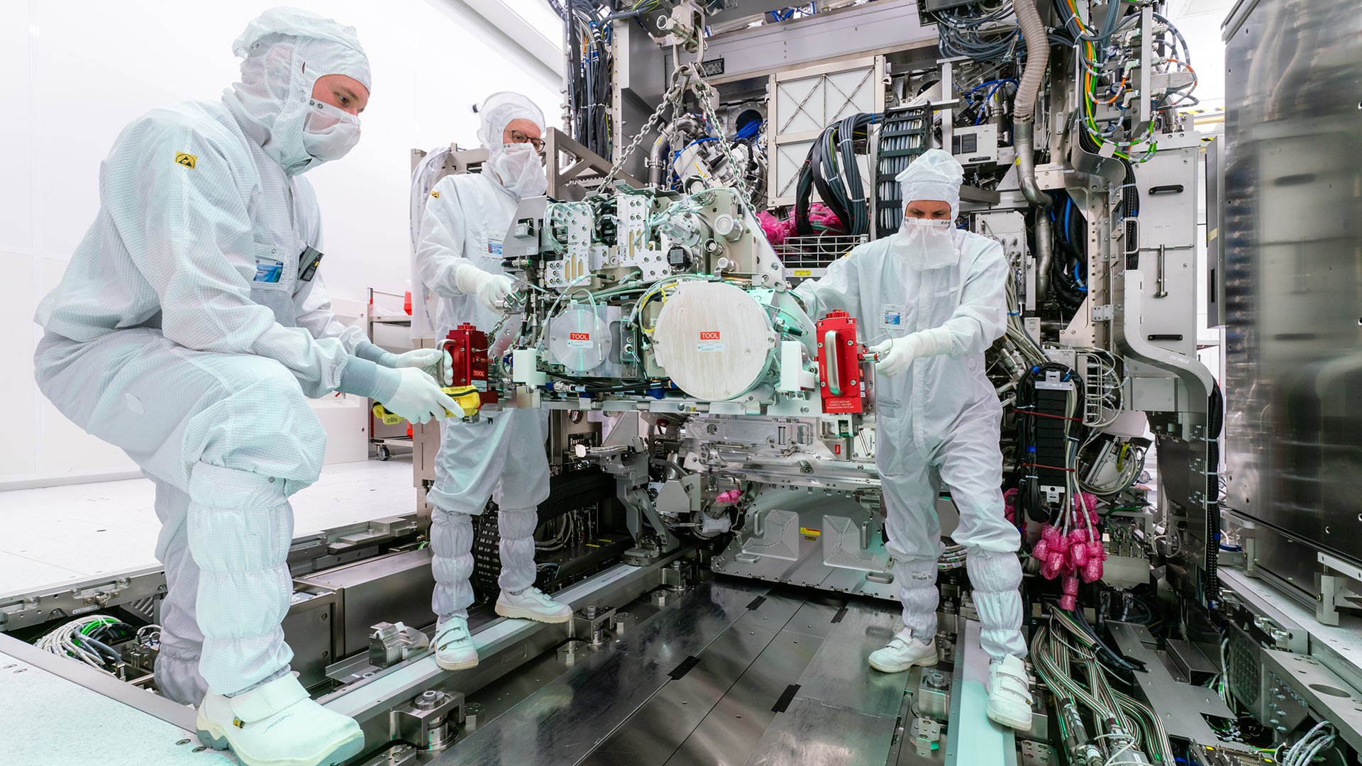 Three people in protective clothing working on a lithography machine