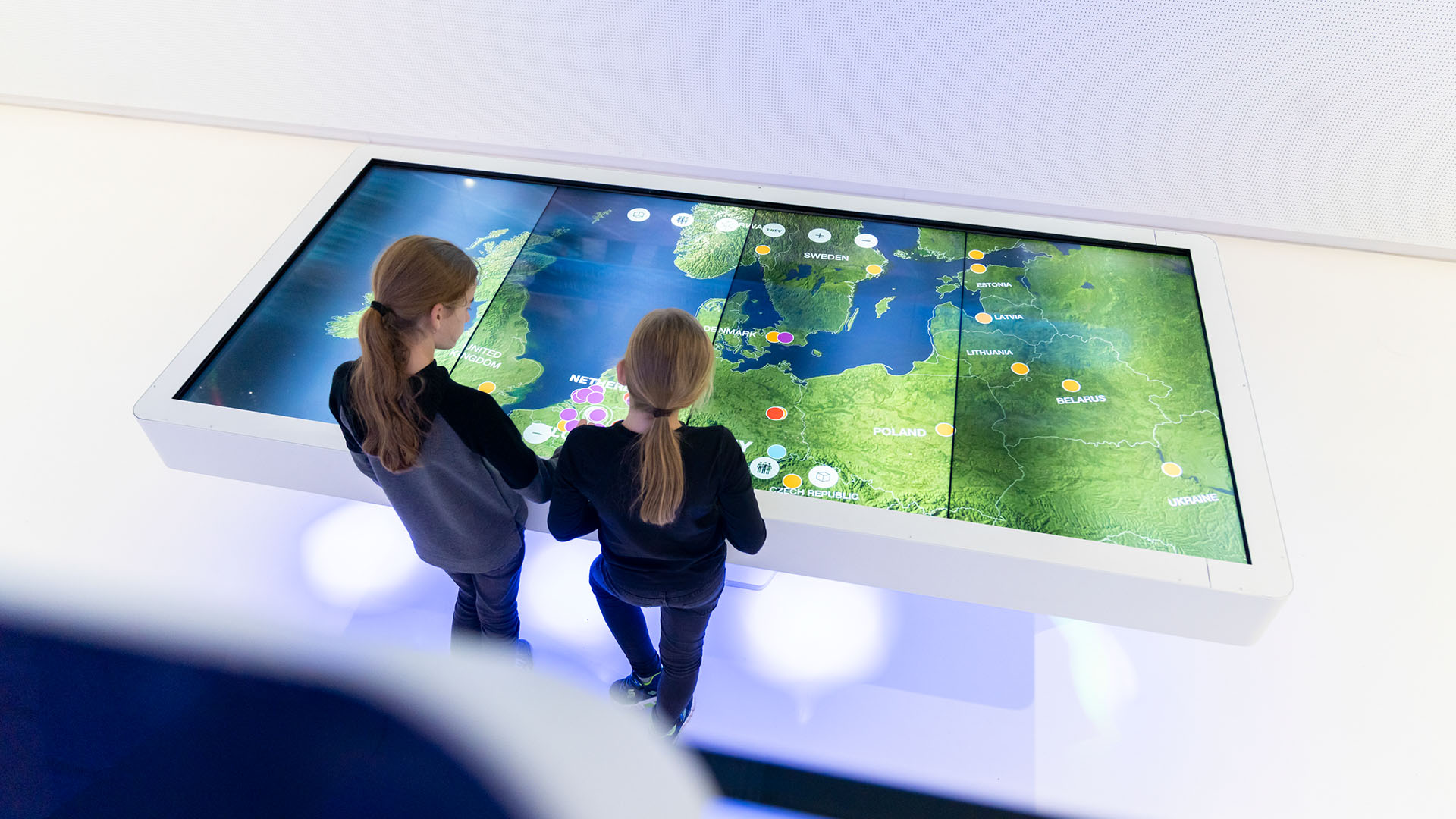 Two people interacting with a large, interactive digital map display at ASML's Experience Center, engaging with geographical information showing various locations and data points. 