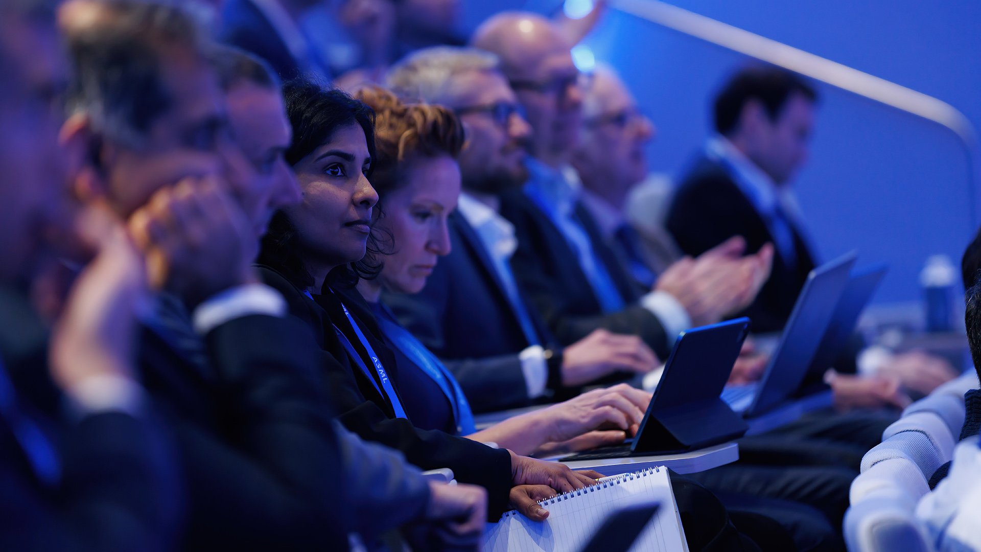Attendees at Investor Day focusing intently on presentations, with some using laptops, captured in an ASML auditorium.