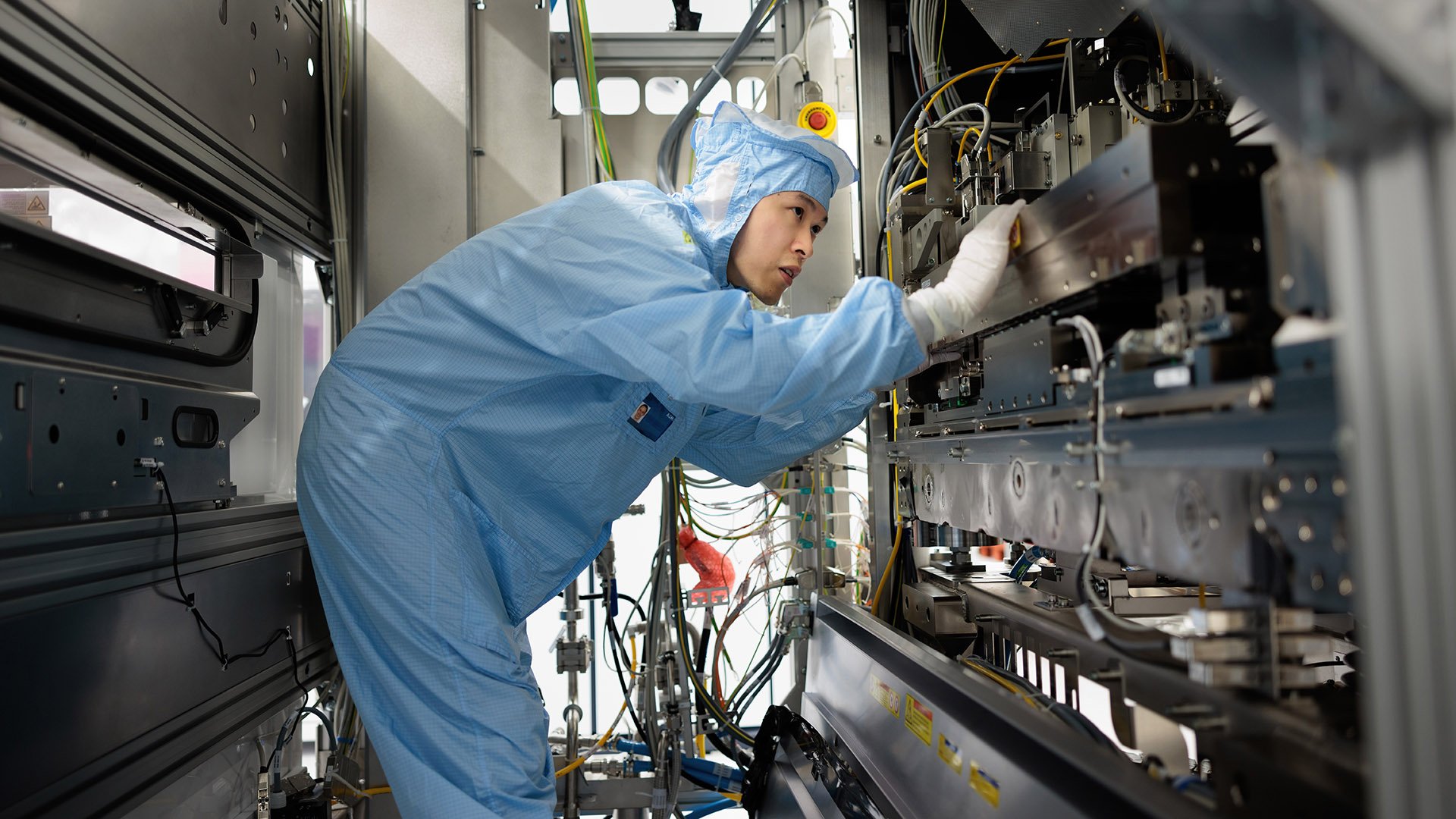 An ASML engineer in a cleanroom suit works on high-tech semiconductor manufacturing equipment.