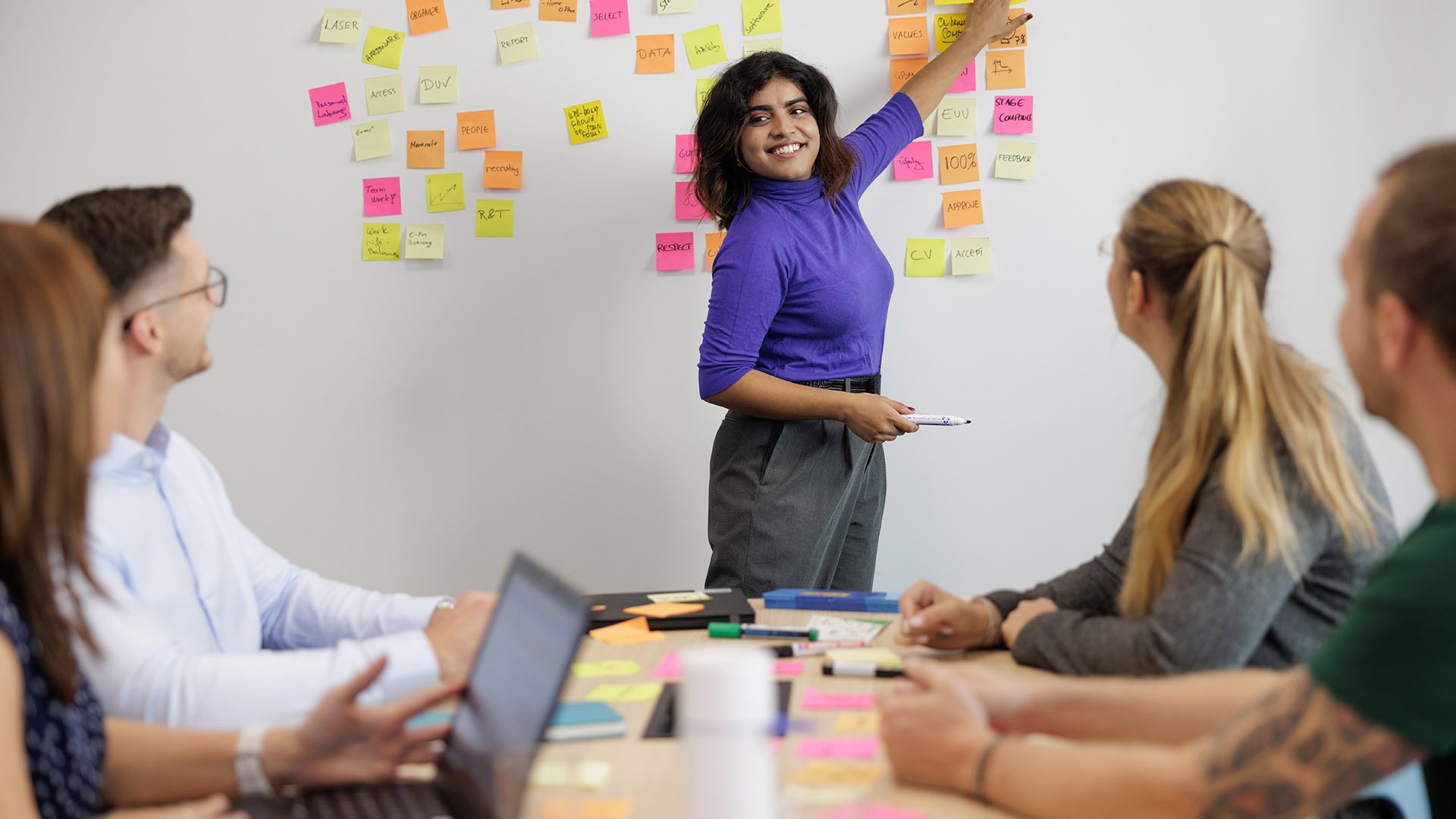 ASML employees are seen having a brainstorming session. A woman is pointing at the sticky notes on a white board. 