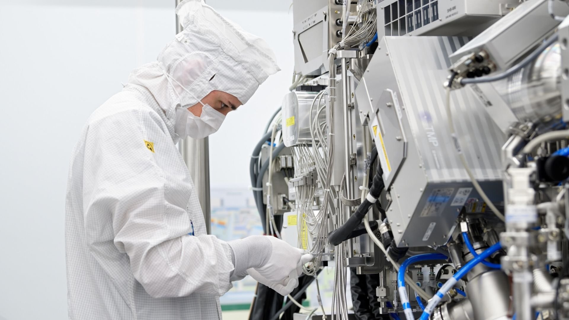 A man in a white cleanroom suit adjusts an ASML lithography machine.
