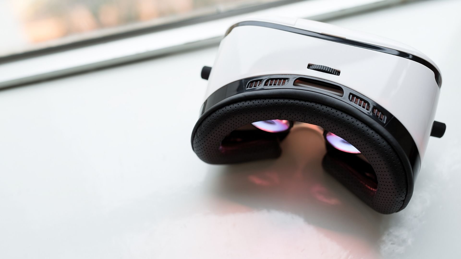 A white VR headset lies on a windowsill. A white VR headset lies on a windowsill.