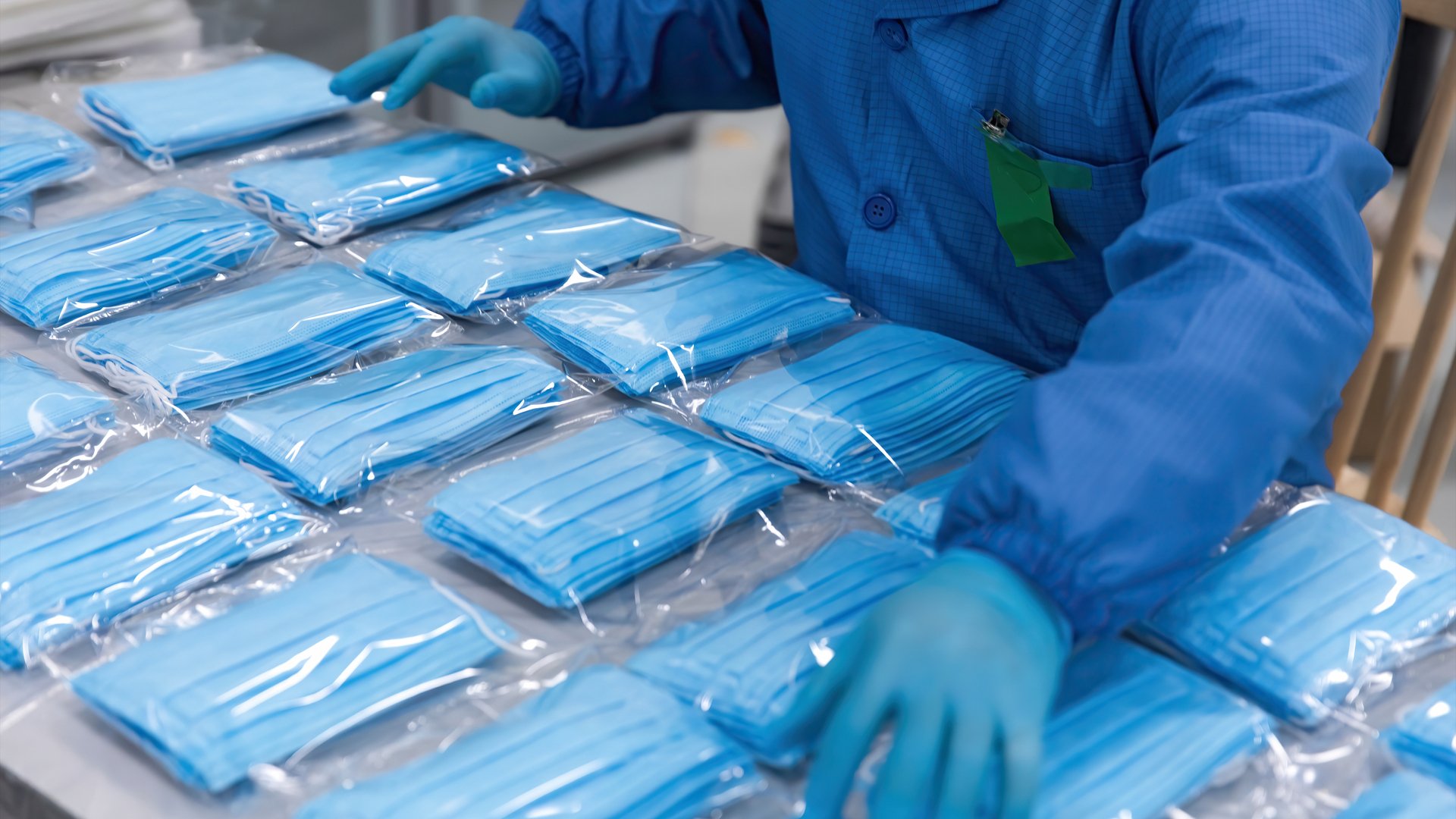A person in blue hospital uniform sorts through packages of face masks.