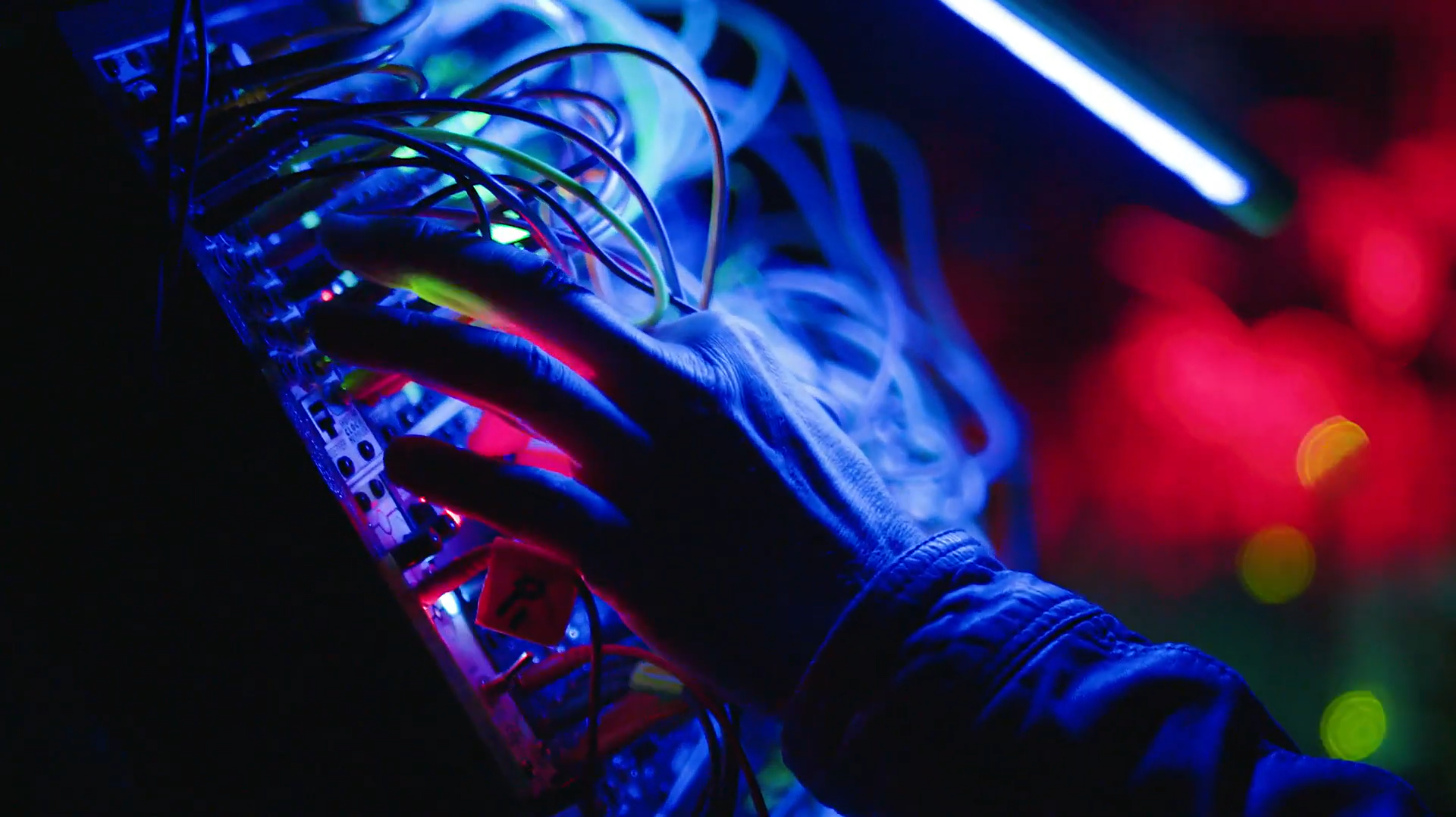 A hand on a glowing wired dashboard with multi-colored lights.