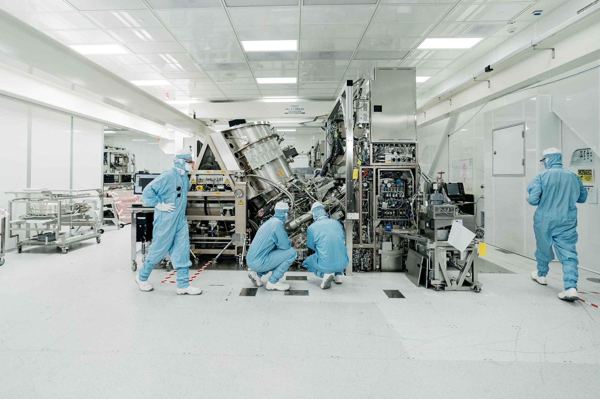 People in cleanroom suits work on an exposed ASML lithography system
