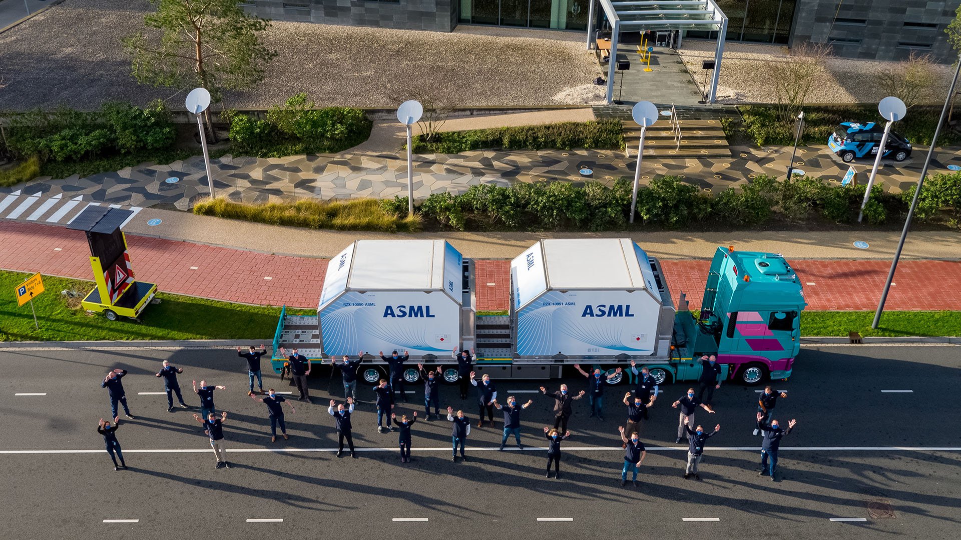 Employees stand with arms raised in front of truck containing the 100th ASML EUV machine