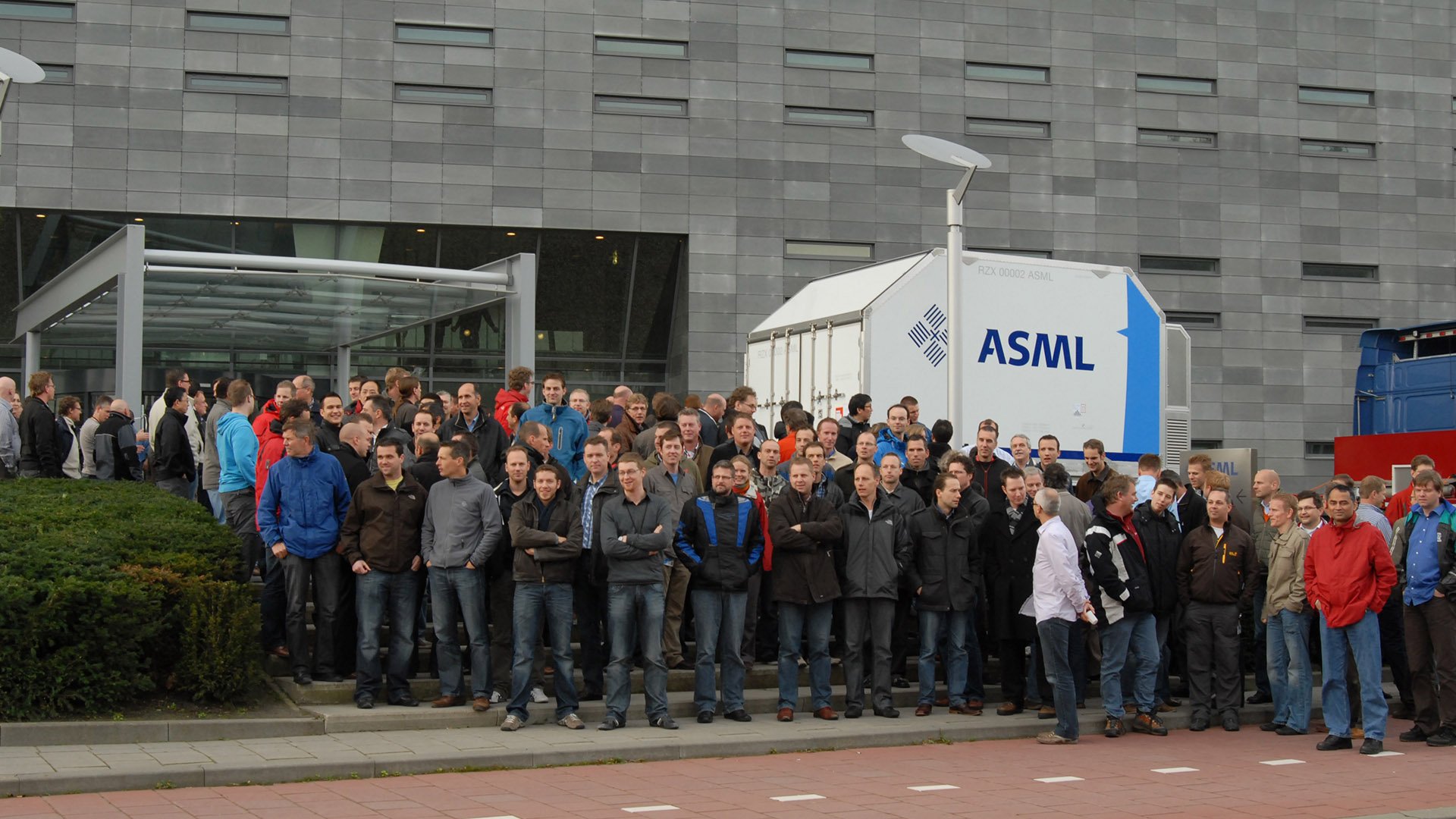 A group of employees stands in front of ASML headquarters in Veldhoven, the Netherlands to celebrate the first EUV machine shipment in 2010.