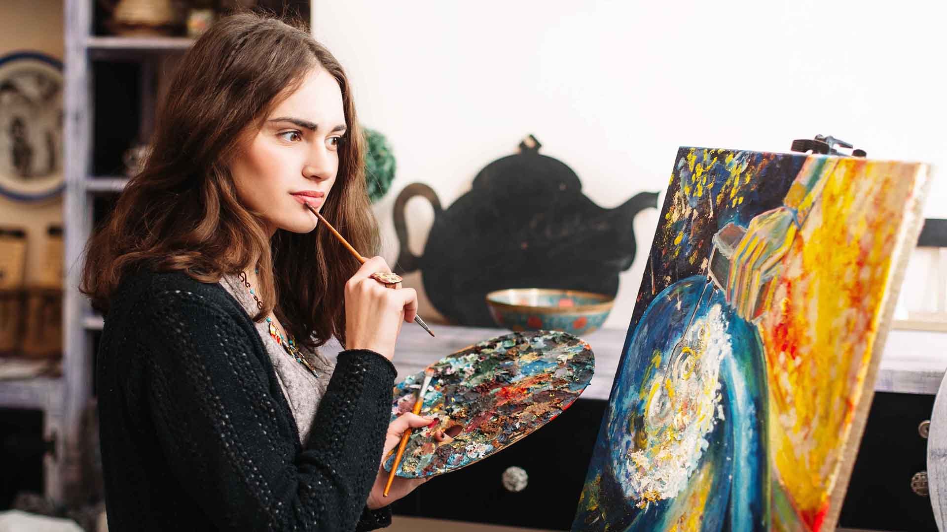 A woman holding a brush and palette in front of a painting.