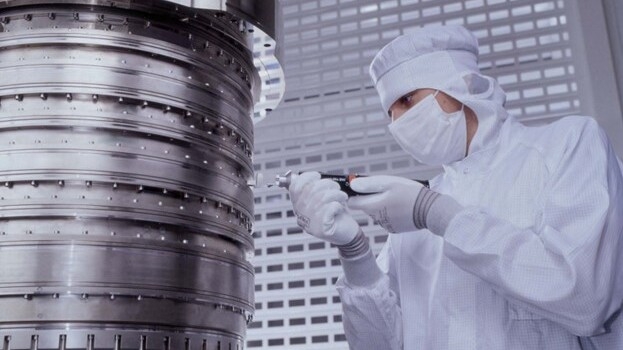 A person in a cleanroom suit makes an adjustment to the ZEISS projection optics system.