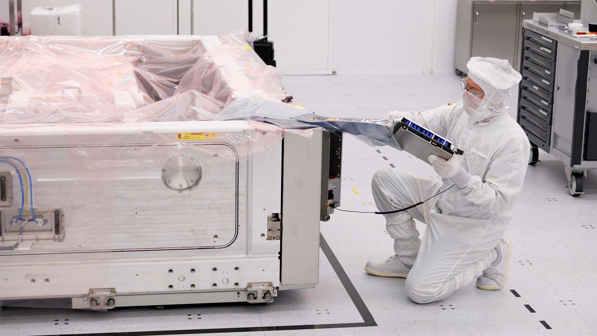A person in a cleanroom dismantles wafer stage for re-use.