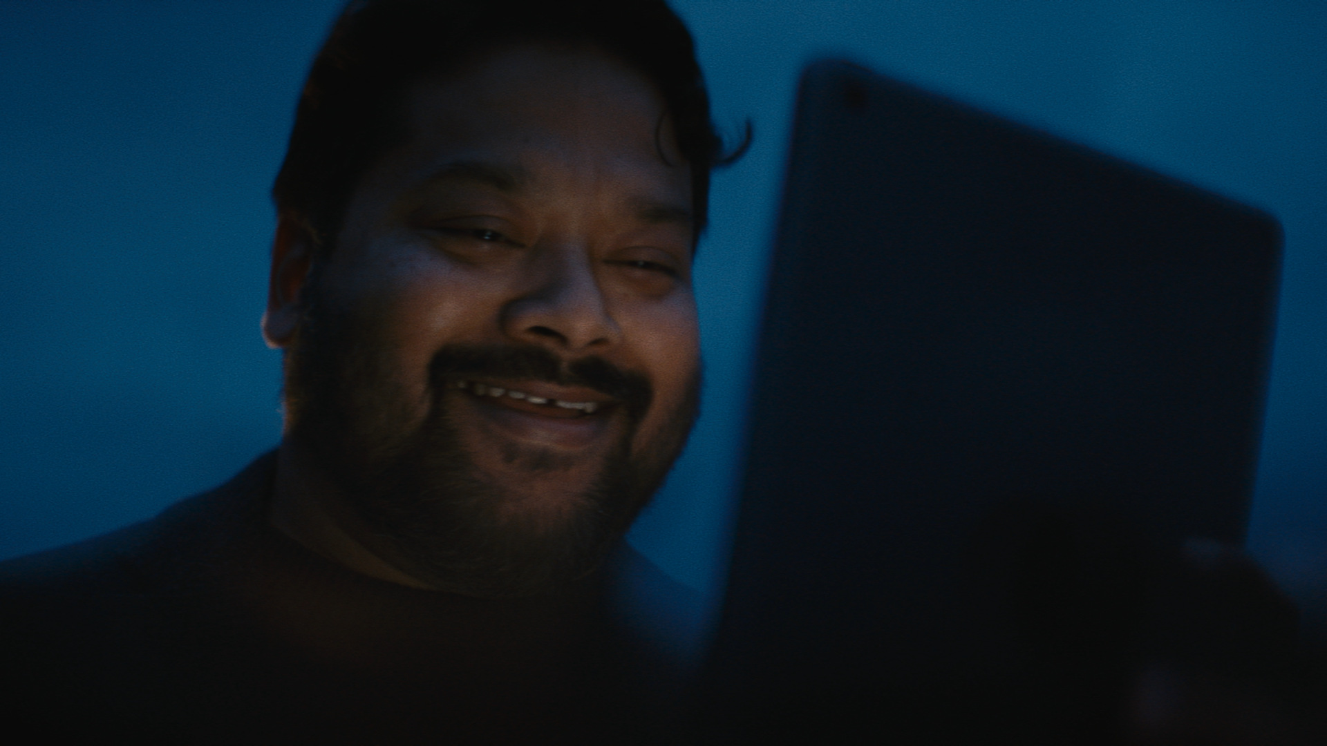 A man smiles as he looks at a tablet that lights up his face.