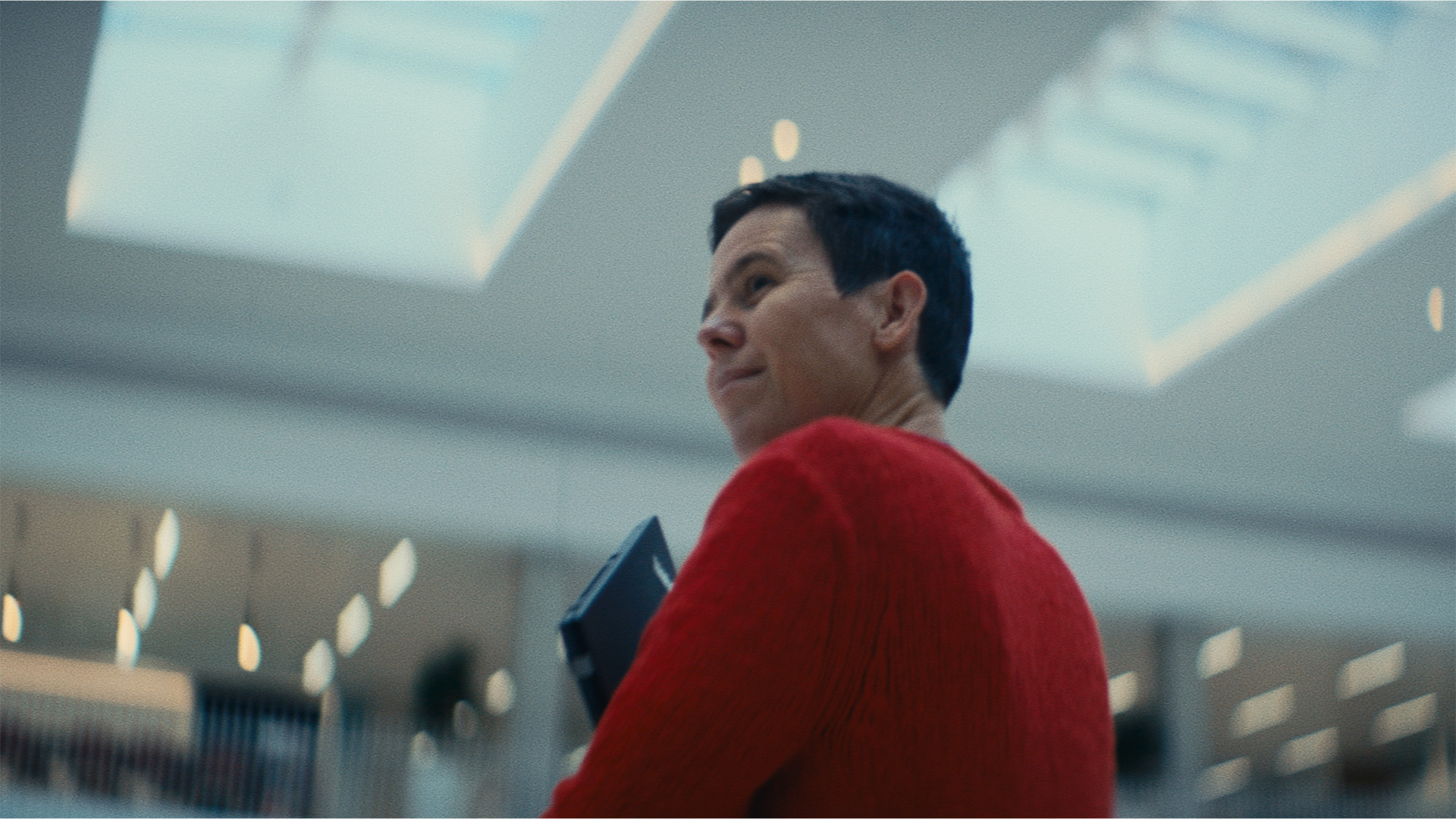 A woman holding a laptop to her chest walks through an indoor plaza with skylights.