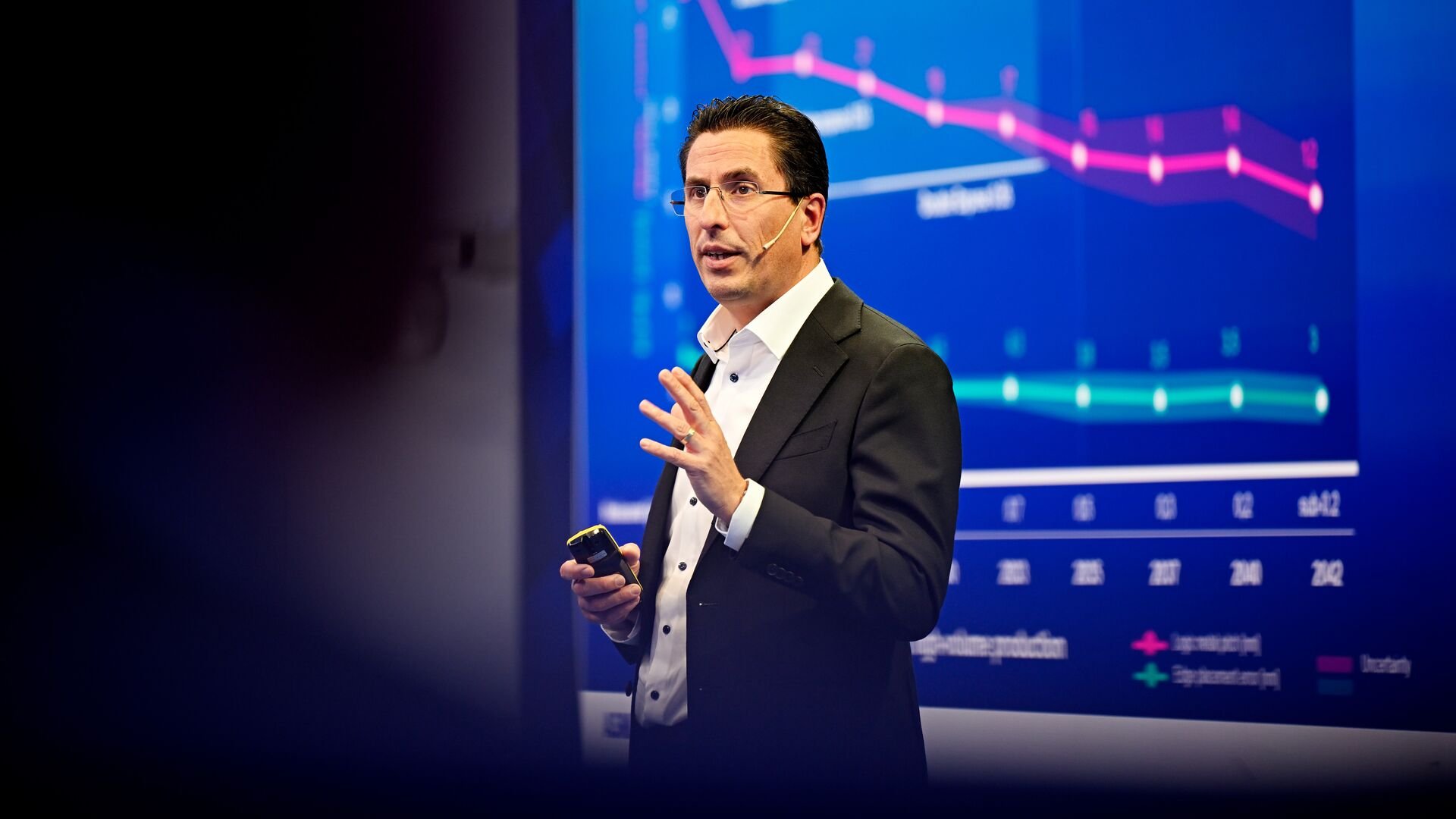 ASML CTO Marco Pieters speaks on stage while standing in front of a blue screen showing a graph.