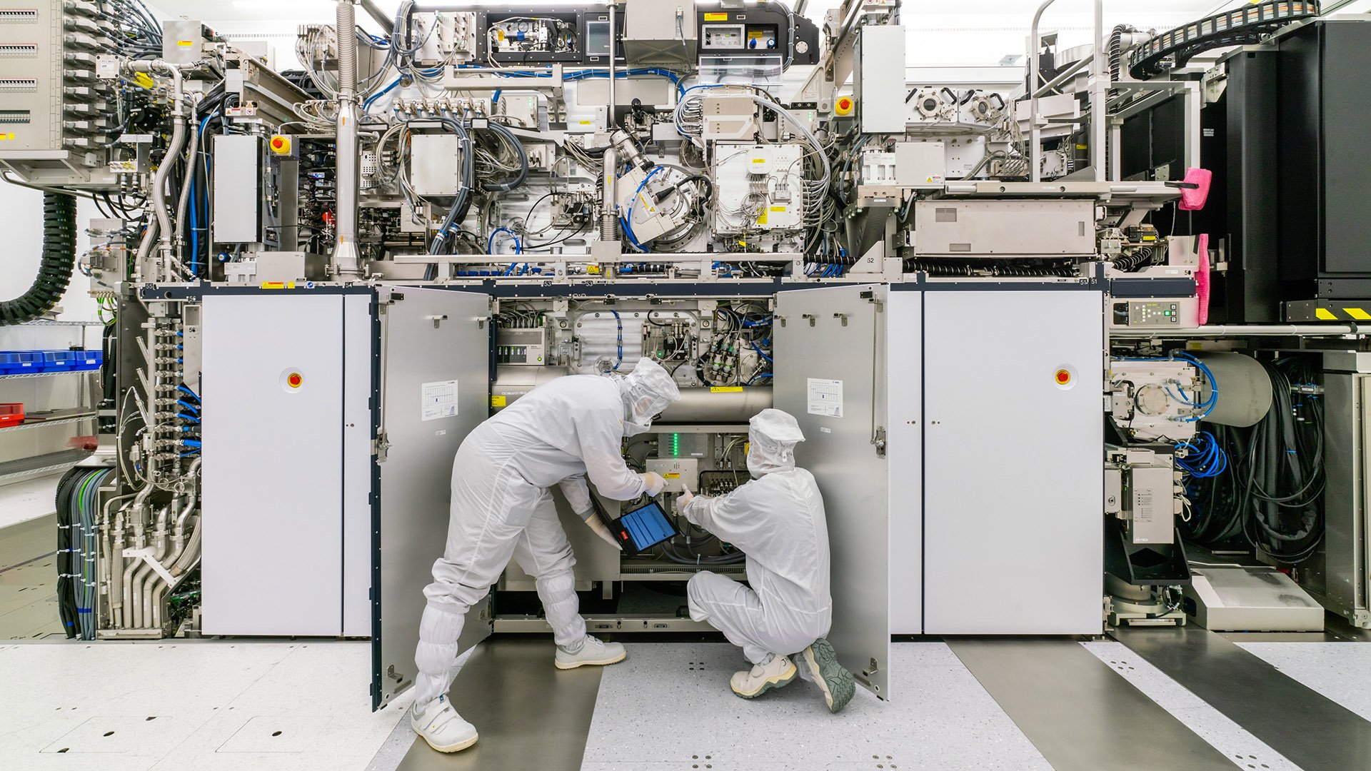 Two people in cleanroom suits working on ASML lithography machine