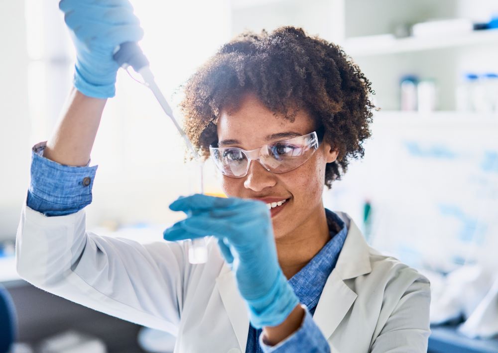 A laboratory medicine professional pipets a sample while smiling.