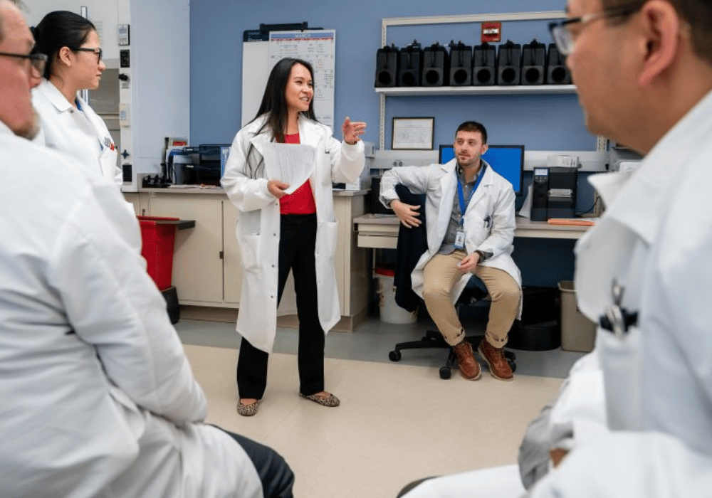 A woman in a lab coat speaks to a crowd of gathered laboratory staff