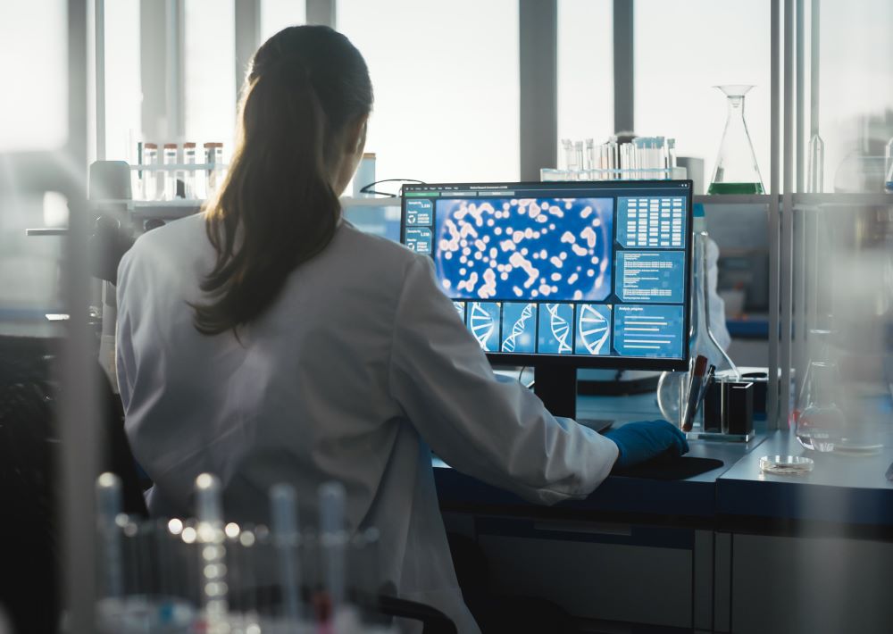 A lab medicine professional works at a computer showing images of cells and DNA.